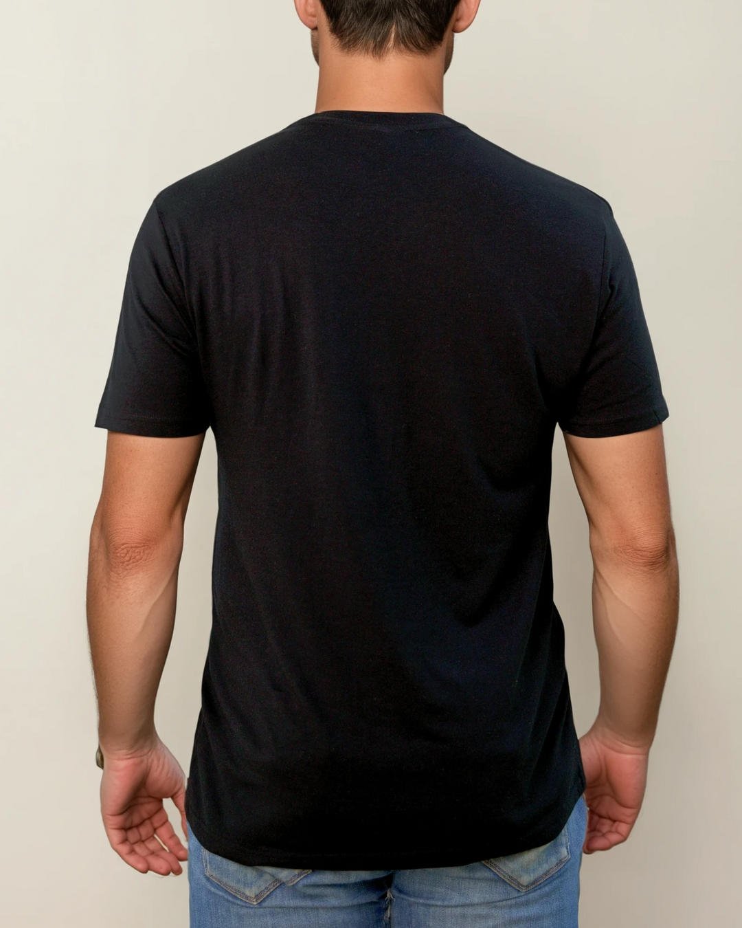 The Ecotton Everyday Tee - Black color, back view of a person wearing paired with blue jeans against a plain gray background. The setting is casual and simple.