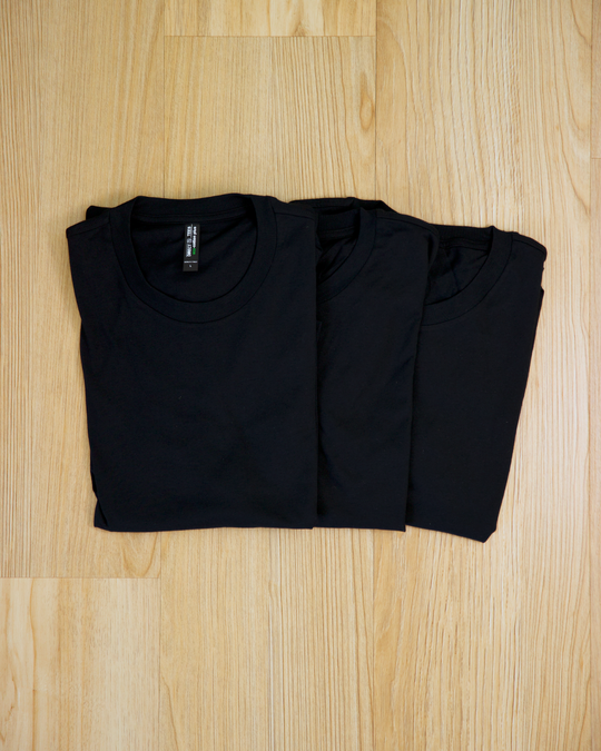 The Ecotton Everyday Tee Black Three pack neatly folded and lies side by side on a light wooden floor, showcasing its simple and minimalist design.