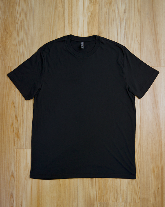 The Ecotton Everyday Tee Black Three pack, neatly laid on a light wooden floor. The shirt is short-sleeved and round-necked, conveying simplicity and minimalism.